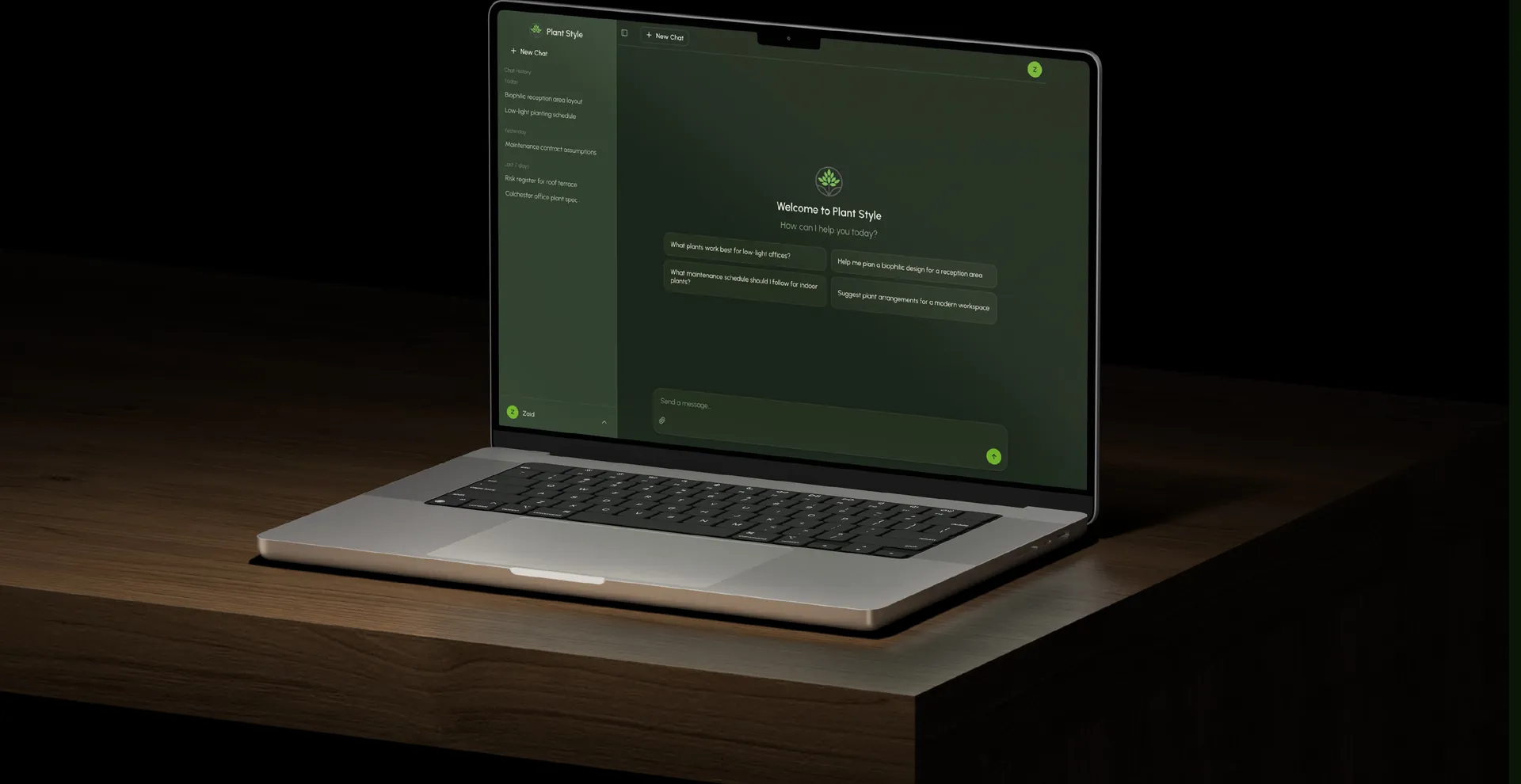 Laptop on a wooden desk showing the chatbot welcome screen with suggested questions
