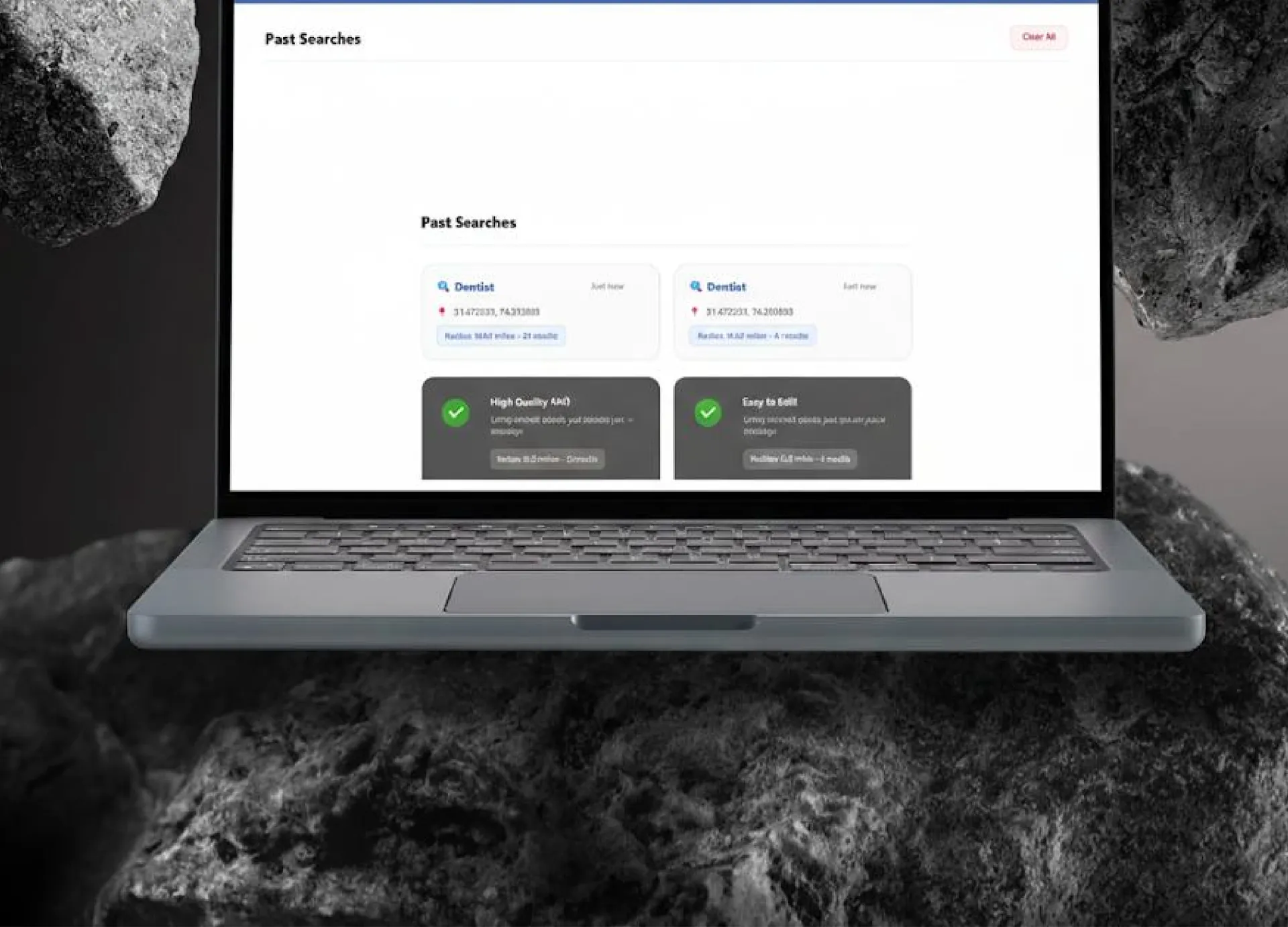 Laptop between dark rocks showing a past searches screen with saved search cards