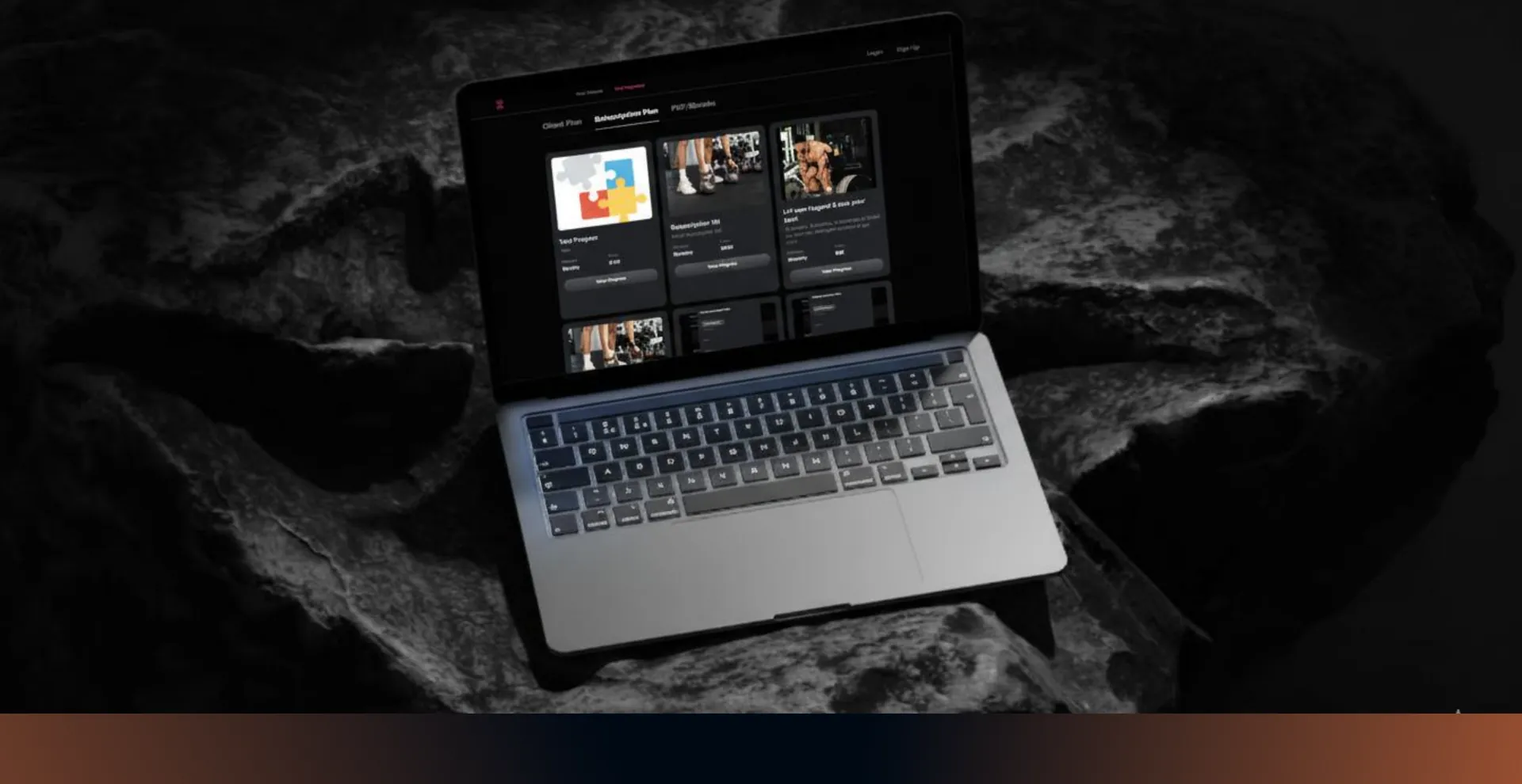 Laptop on dark rock showing workout program cards with photos